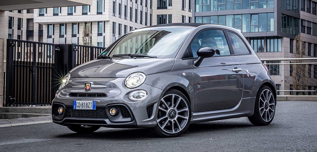 Ein grauer Abarth 595C steht auf einer Straße in einer Stadt.