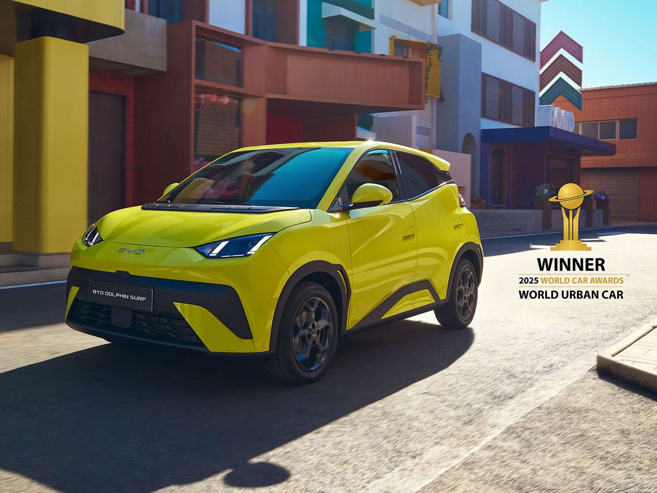 Grüngelbes Auto BYD Dolphin Surf fährt über eine Straße durch die Start, rechts daneben Darstellung eine Auszeichnung Wolrd Urban Car Winner 2025