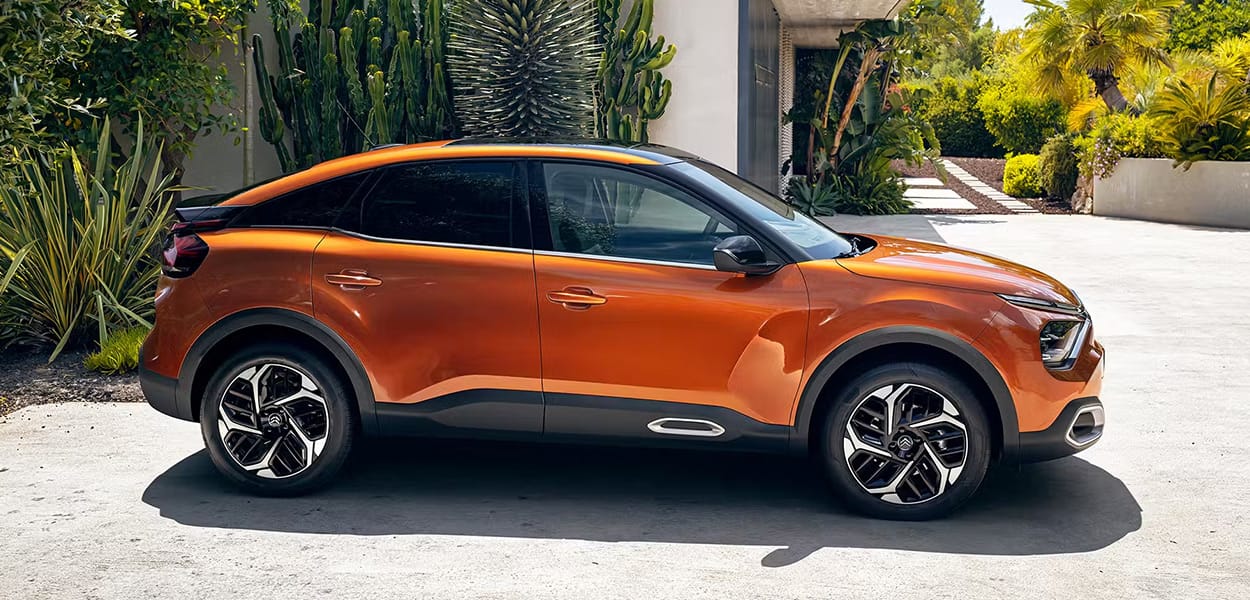 Ein orangener Citroen C4 mit Seitenansicht steht vor einer mediterraner Kulisse.