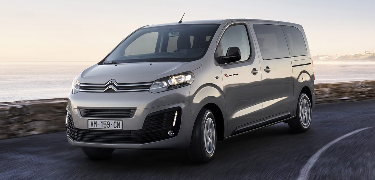 Ein silbergrauer Citroen Spacetourer fährt auf einer Straße am Meer entlang.