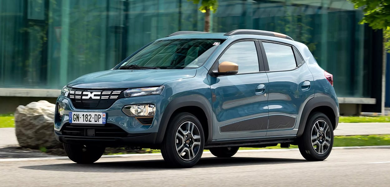 Ein blauer Dacia Spring mit goldenen Seitenspiegeln fährt durch eine Stadt. 