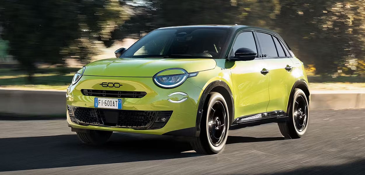 Ein grüngelber Fiat 600 fährt auf einer Straße.