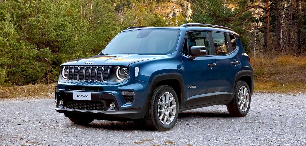 Ein blauer Jeep Renegade steht auf einem Schotterweg am Wald.