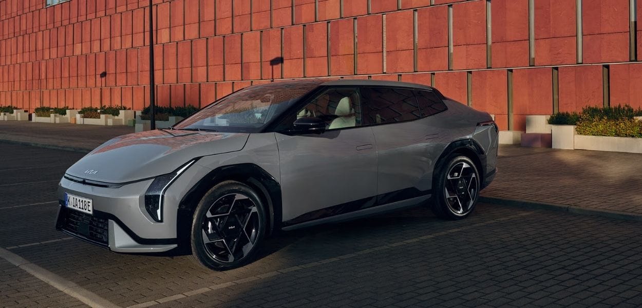 Grauer Kia EV4 in Seitenansicht auf einem Parkplatz vor einer modernen Backsteinfassade – elegantes Elektrofahrzeug im urbanen Umfeld.