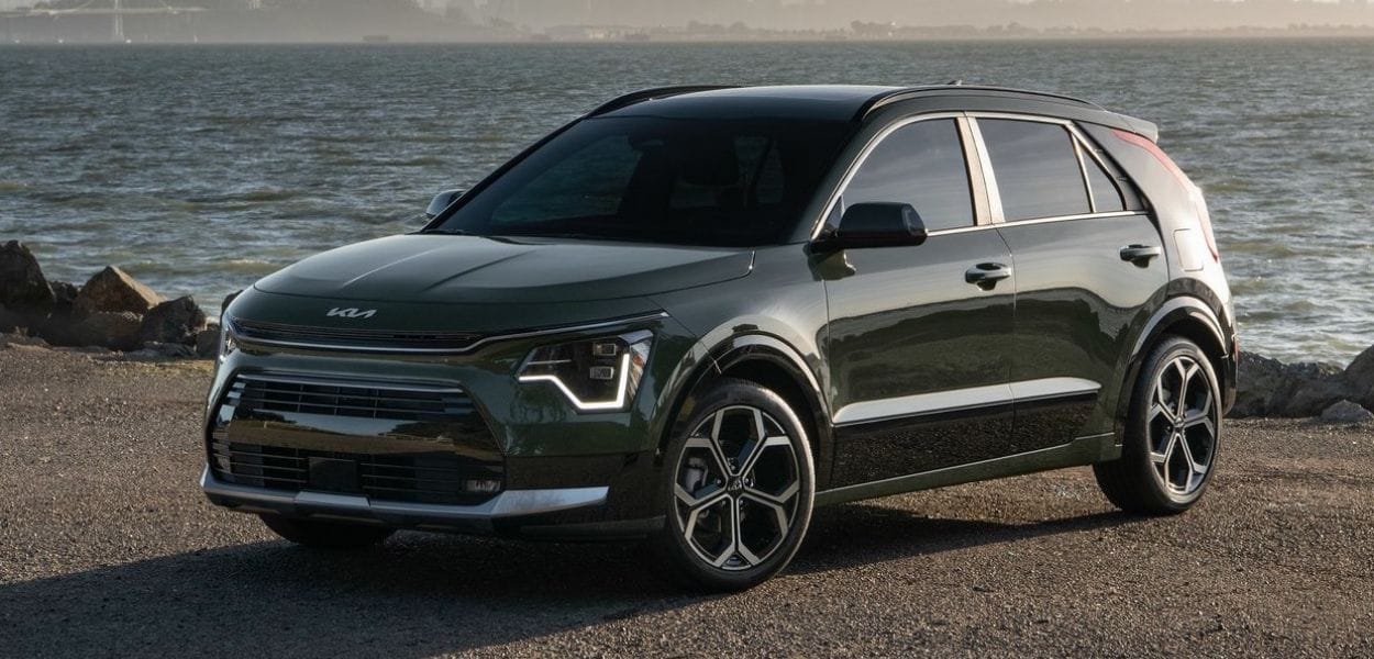 Dunkelgrüner Kia SUV am Ufer mit Wasser und felsiger Küste im Hintergrund.