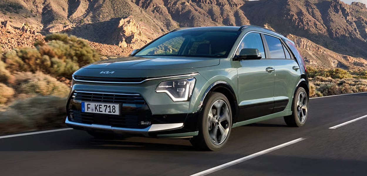 Ein grüner Kia Niro fährt über eine Landstraße vor eine Bergkulisse. 