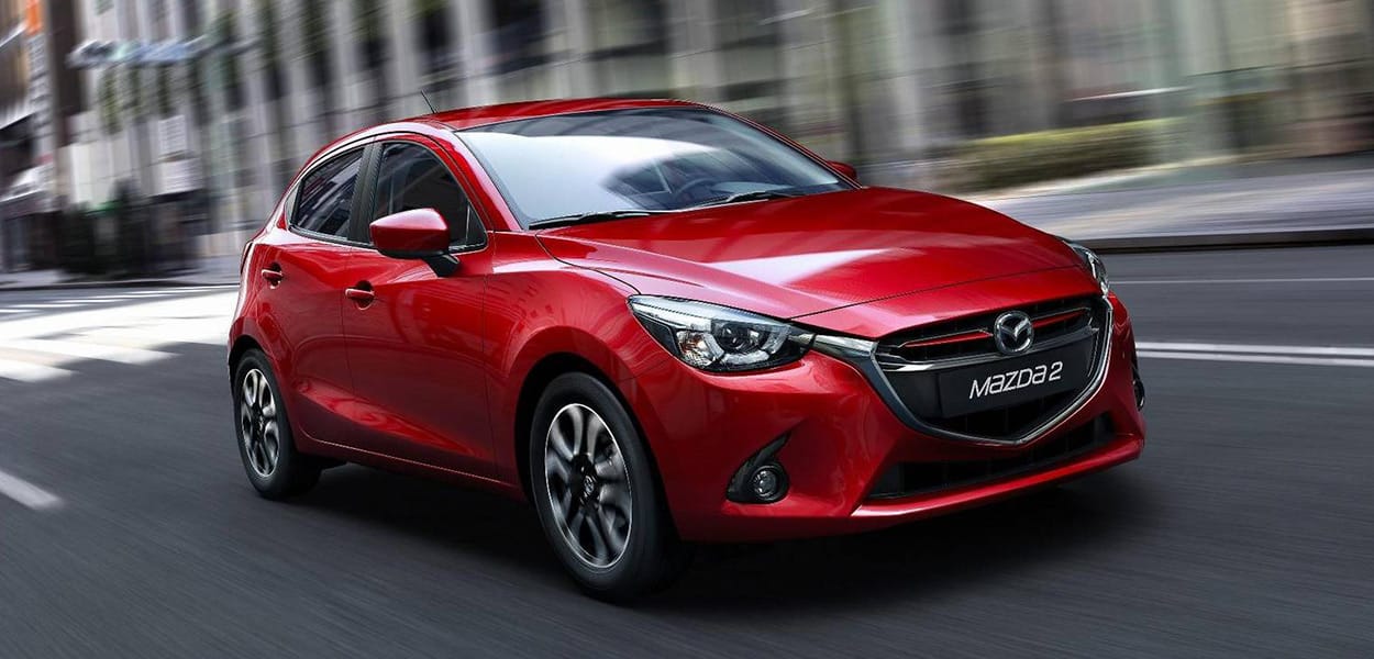 Ein roter Mazda 2 fährt durch eine moderne Stadt.