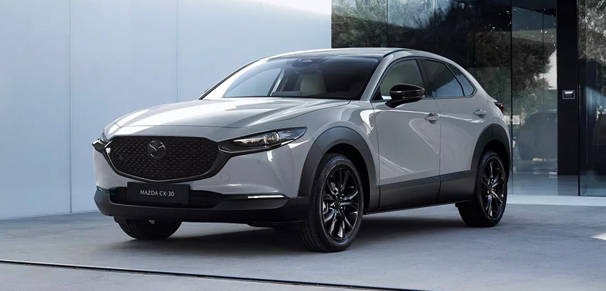 Ein grauer Mazda CX-30 steht auf einem Parkplatz vor einem modernen Bürogebäude.