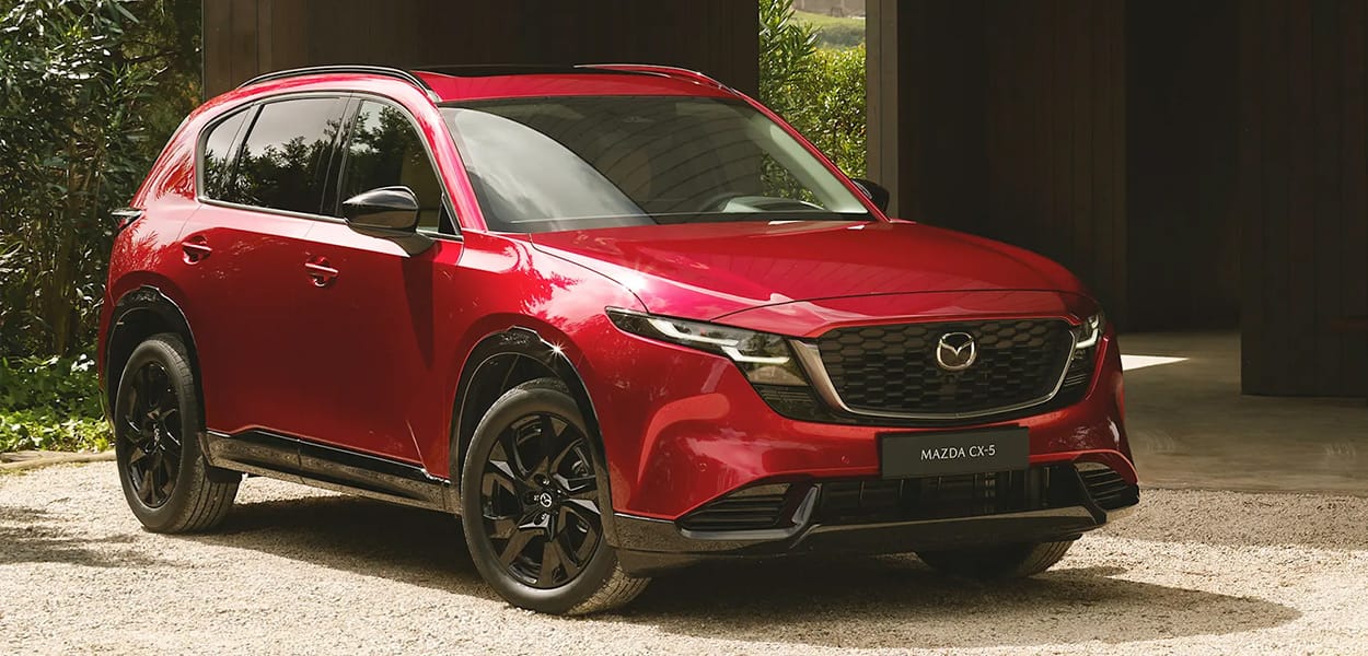 Ein roter Mazda CX-5 SUV steht auf einem Schotterplatz vor einem Gebäude.