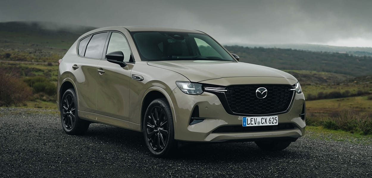 Ein olivgrüner Mazda CX-60 steht auf einem Weg in einer weiten Landschaft.