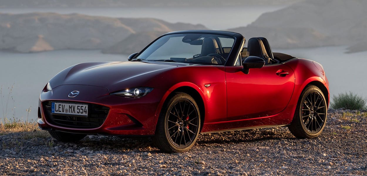 Ein roter Mazda MX5 steht auf einem Schotterplatz am Meer.