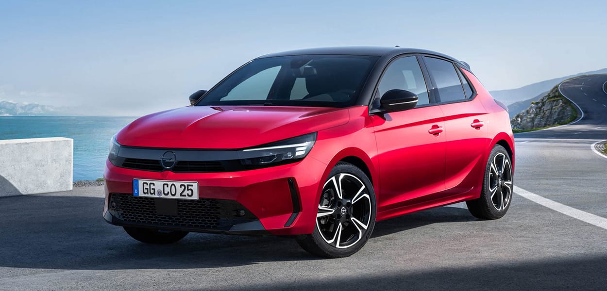 Ein roter Opel Corsa mit schwarzem Dach parkt an einer Landstraße am Meer.