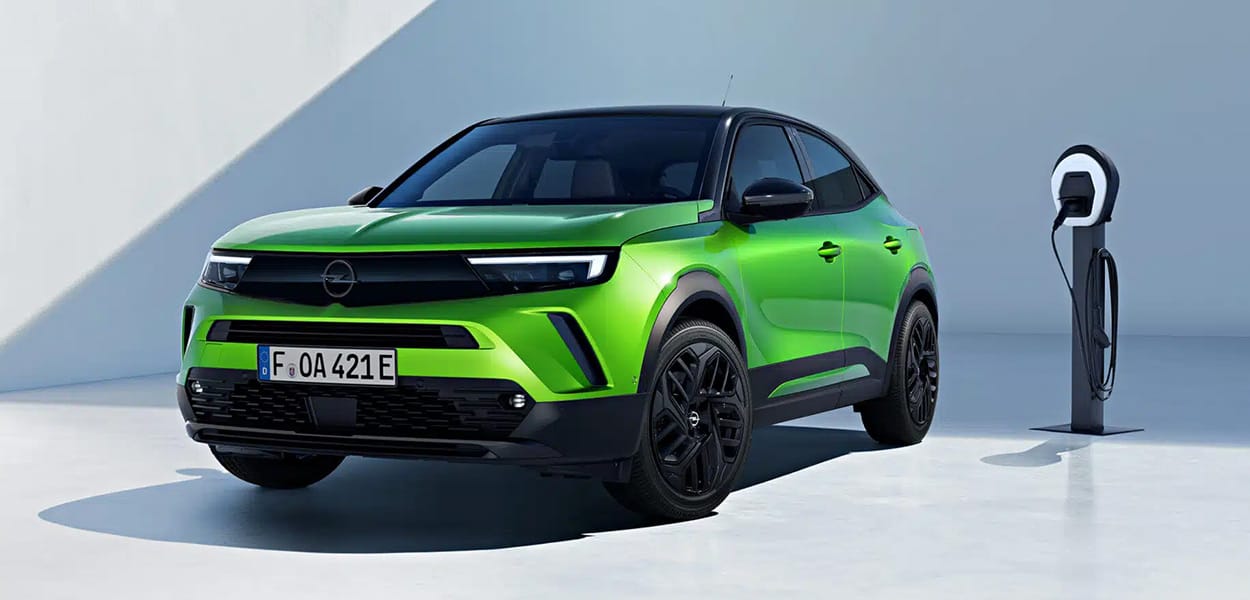 Ein grüner Opel Mokka e mit schwarzem Dach steht an einer Ladesäule an einer hellen Wand.