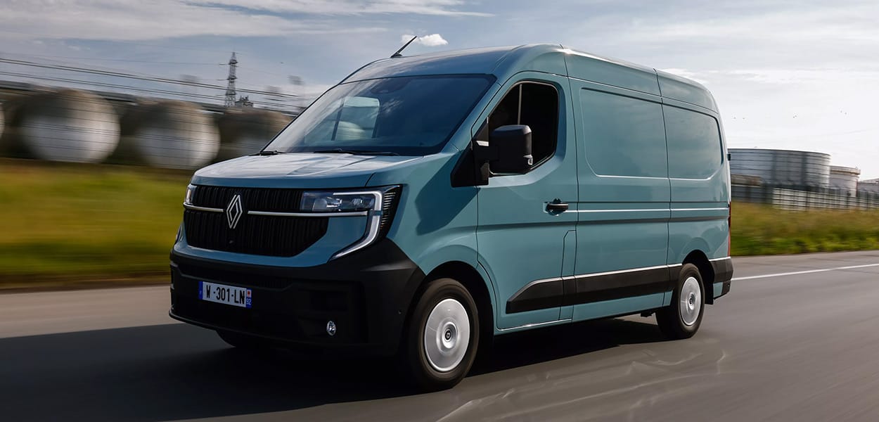 Ein türkisfarbener Renault Master Transporter fährt über eine Straße an einem Industriegelände vorbei. 