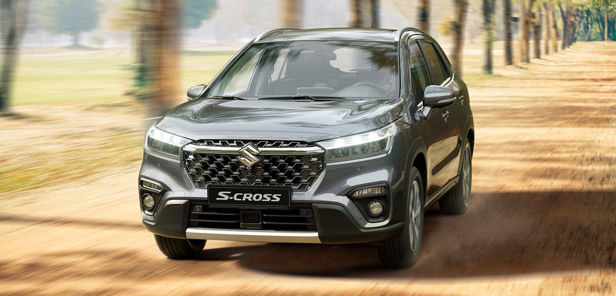 Ein silbergrauer Suzuki S-Cross fährt über eine mit Bäumen besetzte Allee.