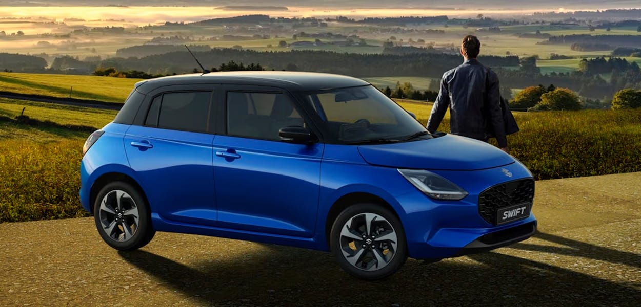 Seitenansicht eines am Weg parkenden blauen Suzuki Swift mit einem Mann, der in die Ferne einer wunderschönen Landschaft schaut.