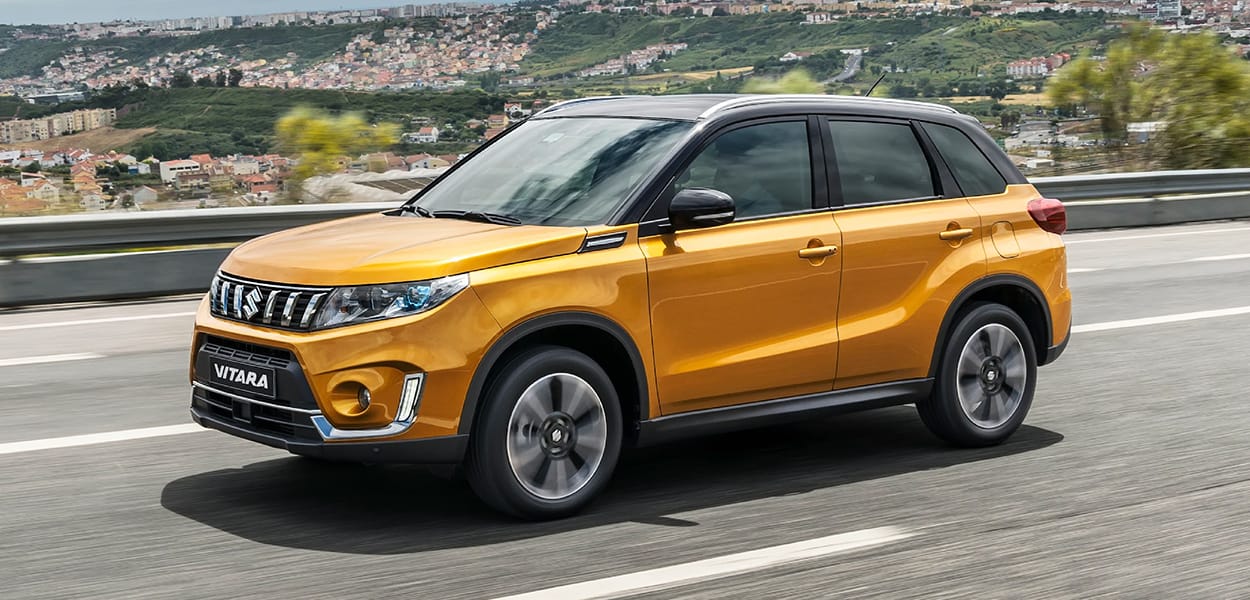 Ein orange-schwarzer Suzuki Vitara fährt auf einer Landstraße.