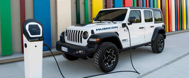 Weißer Jeep Wrangler vor einer bunten Wand wird an einer Elektro-Säule geladen.